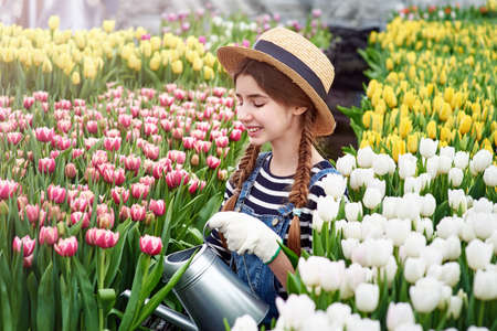 Happy smiling teenager girl in hat with watering can in blossoming tulip gardenの写真素材