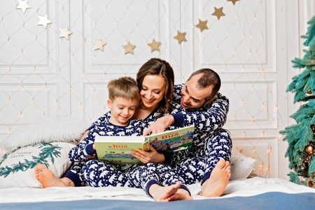 Happy family in pajamas reading book with their child boy near decorated Christmas tree.の写真素材