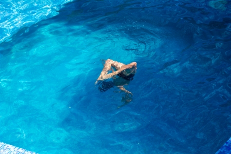 Boy swims and dives into the bright blue pool waterの写真素材