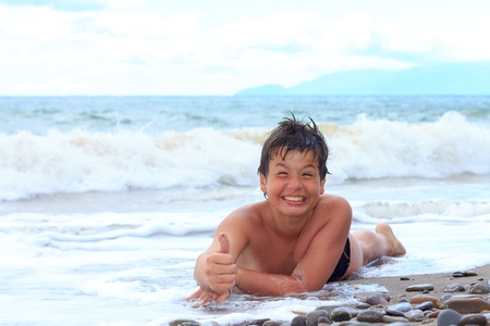 happy laughing boy of twelve showing thumbs up sign on the sea beachの写真素材