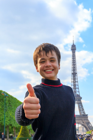 Cheerful teenager shows thumb up sitting on the Esplanade des Invalides in Paris , Franceの写真素材