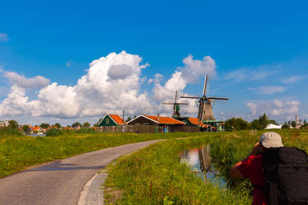 Photographer takes  picturesque rural landscape with windmills in Zaanse Schans close to river, Holland, Netherlandsの写真素材