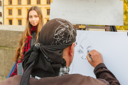 Prague, Czech Republic - October 6, 2014: Street artist paints a portrait-caricature of a beautiful girl on the Charles Bridge. Shallow depth of field, focus on the portraitのeditorial素材