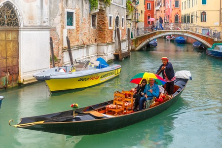 Venice, Italy - May 23, 2015: Happy tourists under bright umbrella ride in Gondola on canal in the rain. Gondola, the symbol of Venice, is a traditional Venetian rowing boat. Now there are 425 hereditary Venice gondoliers with their own courts.のeditorial素材