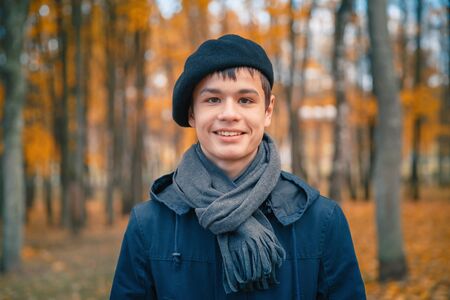 Happy smiling teenage boy in a beret and jacket in the autumn sunny parkの写真素材