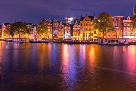 Amsterdam canal Amstel with typical dutch houses and houseboats with multi-colored reflections at night, Holland, Netherlands.の写真素材