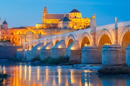 Illuminated Great Mosque Mezquita - Catedral de Cordoba with mirror reflection and Roman bridge across Guadalquivir river during evening blue hour, Cordoba, Andalusia, Spainの写真素材