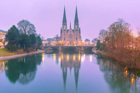 Picturesque foggy Reformed Saint Paul church with mirror reflections in the river Ile during morning blue hour, Strasbourg, Alsace, Franceの写真素材