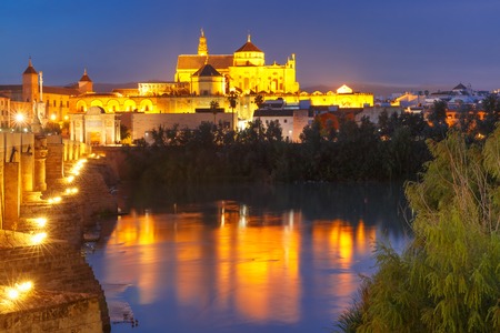 Illuminated Great Mosque Mezquita - Catedral de Cordoba with mirror reflection and Roman bridge across Guadalquivir river during evening blue hour, Cordoba, Andalusia, Spainの写真素材