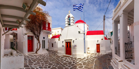 Agia Kyriaki Church, typical Greek church building and Large waving Greek flag against the blue sky on the island Mykonos, The island of the winds, Greeceの写真素材