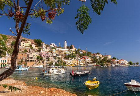 Hillside view of the colorful buildings and busy harbor on Symi Island, Greece.