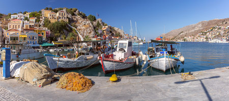 Panoramic view of colorful fishing harbor lined with traditional boats on Symi Island, Greece