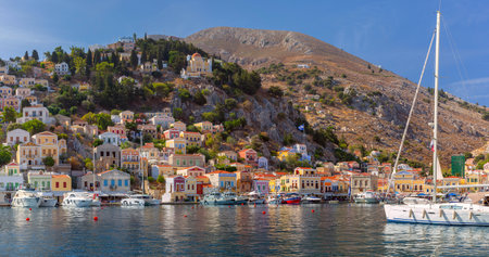 Hillside view of the colorful buildings and busy harbor on Symi Island, Greece.の写真素材