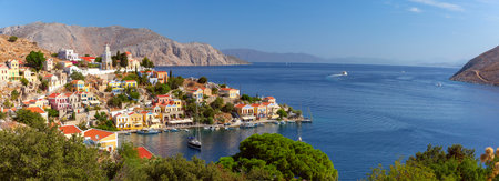 Wide panoramic shot of Symi Island with colorful houses against scenic mountain backdrop, Greeceの写真素材