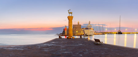 View of Mandraki Harbour with deer statue, lighthouse, yachts and fortress in Rhodes city, Greece at sunsetの写真素材