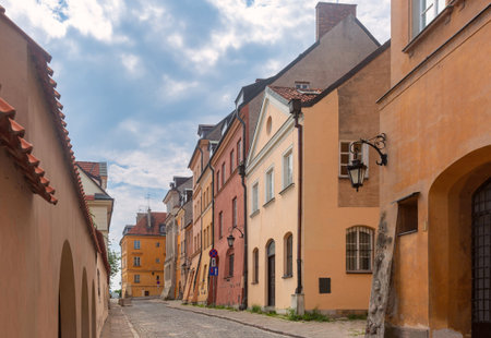 Historic cobblestone street in Old Town, Warsaw, Poland, lined with colorful residential buildings under a cloudy skyの写真素材