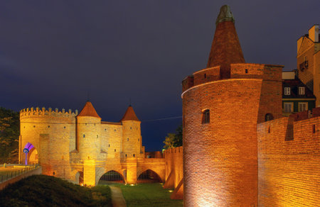 Illuminated medieval Warsaw Barbican in Old Town, Warsaw, Poland, captured at night with brick walls and towersの写真素材