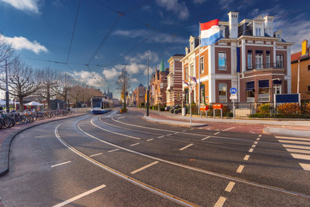 Tram passing a historic building with Dutch flag on a sunny street in Amsterdam, Netherlandsの写真素材