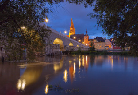 Stone Bridge and cathedral in Regensburg illuminated at night above the Danube River.の写真素材