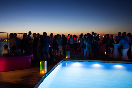 Party crowd of people having fun at roof top club with pool at sunset