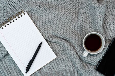 Flatlay of Cosy working writing place with warm sweater coffee, note paper and phone. work from home. Writing.の写真素材