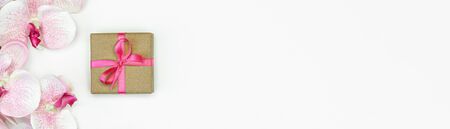 banner of Gift present box with pink ribbon with orchid flowers on white background flat lay.spring concept. Copy spaceの写真素材