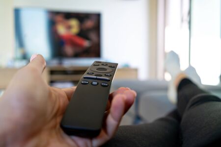Watching TV, hand holding remote controller in front of big televisionの写真素材