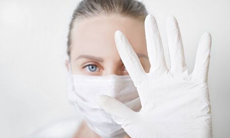 Stop coronavirus covid-19 pandemic. woman in white medical protective mask and gloves showing gesture stopの写真素材