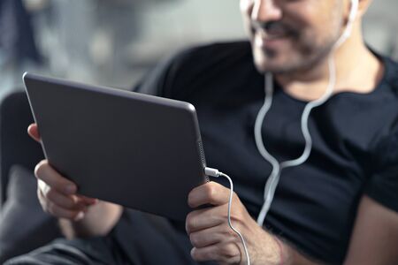 man holding using digital tablet and headphones sitting on a sofa. Online education, working, video call with friends or video conferenceの写真素材