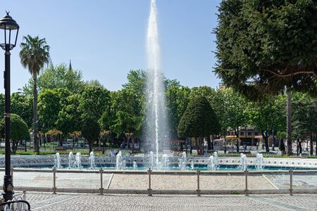 Fountain in city park with green trees at sunny day.の写真素材