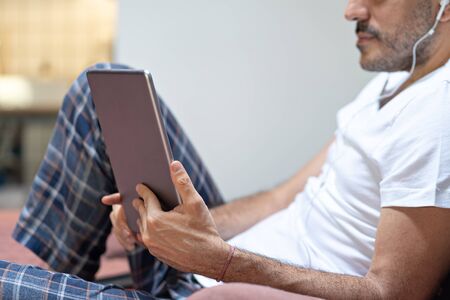 man holding using digital tablet and headphones in bed at home with pijama. Online education, working, video call.の写真素材