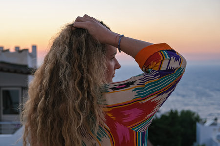 close up of woman from back with hand in hair watching sunset and sea view from terrace of luxury...