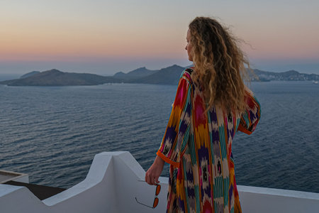 Woman on balcony terrace looking at the beautiful colorful sunset and sea. view from back