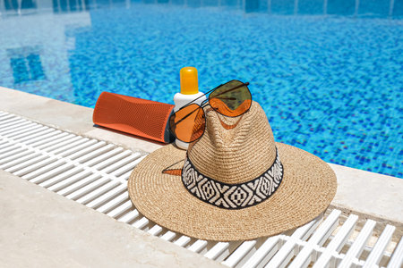 orange coloured beach accessories near swimming pool. Sun cream, sunglasses, music speaker and straw...