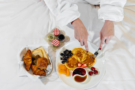 woman eating breakfast in bed. Fresh croissant bread fruits in plate