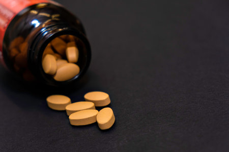 Close-up yellow capsules pill vitamins tablet and jar bottle supplements on black background