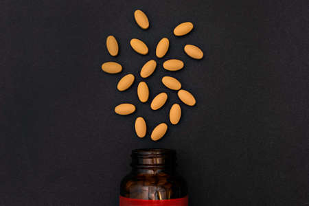 Close-up yellow capsules pill vitamins tablet and jar bottle supplements on black backgroundの写真素材