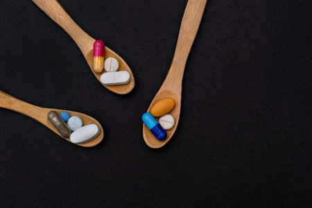 Close-up colorful powder soft capsules pill vitamin in wooden spoon. blue pink yellow brown supplement black backgroundの写真素材