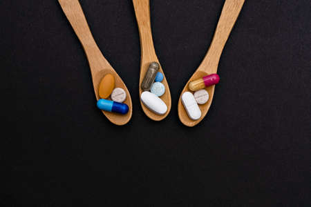 Close-up colorful powder soft capsules pill vitamin in wooden spoon. blue pink yellow brown supplement black backgroundの写真素材