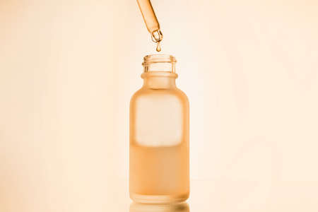 face serum oil drop with dropper glass bottle pipette on yellow background close upの写真素材