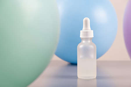 face serum oil dropper glass bottle with pipette with colored balloons background close upの写真素材