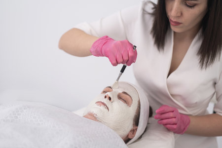 in beauty salon, a woman takes facial care treatment that includes nourishing face peeling mask, expertly applied by a skilled beautician. The close-upの写真素材