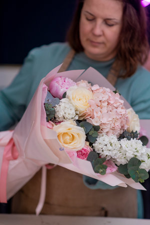 Working in modern floral shop, creative female business owner arranges a stunning bouquet of pink blooms, love for flowers and design.の写真素材