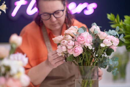 Working with delicate pink roses and peonies, the talented female florist crafts a breathtaking arrangement that is both timeless and memorable.の写真素材