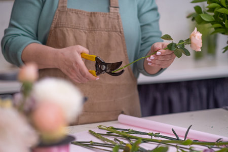 A talented florist, a young woman in her apron, choosing flowers and green leaves carefully crafting...