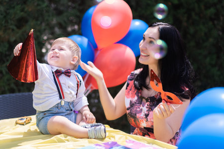 Joyful one-year-old baby, donning a Happy Birthday hat, marks their first year with an outdoor...