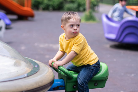 Adorable little boy with Down syndrome spinning on Merry-go-round carousel on playground in city...