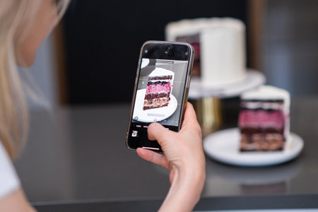 Hand of food blogger holding phone taking picture of piece of homemade shortcake on plate on kitchen table woman capturing finished pastry on camera to show on social media closeupの写真素材