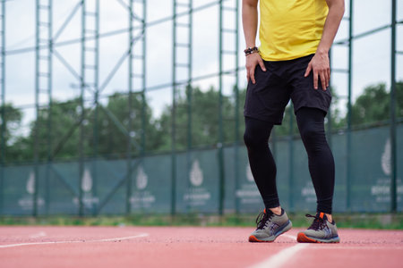 Sportsman in leggings and shorts training on running track with rubber surface and white lines on urban sports arena jogger exercising at stadium closeupの写真素材