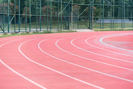 All-weather running track with red rubberized surface separated by white marking lines for athletics training at contemporary sports ground in urban park on summer dayの写真素材